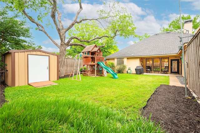 view of yard with an outdoor structure, a fenced backyard, a playground, and a storage unit
