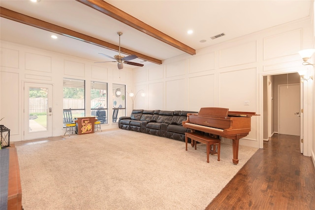 living area with a decorative wall, a ceiling fan, dark wood-type flooring, beamed ceiling, and visible vents