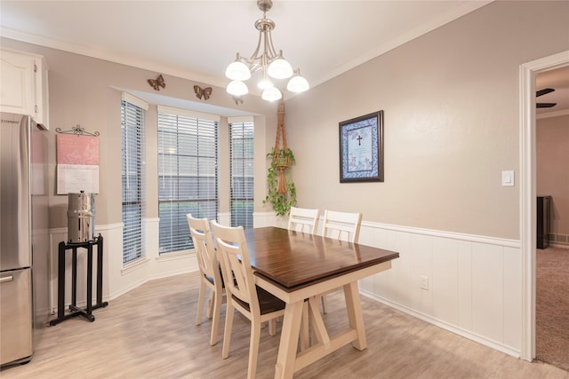 dining space with an inviting chandelier, ornamental molding, light wood-style flooring, and a wainscoted wall