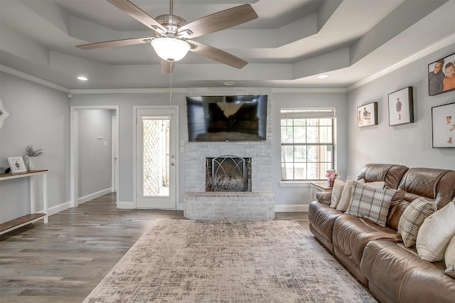 living room featuring a brick fireplace, wood finished floors, and a raised ceiling