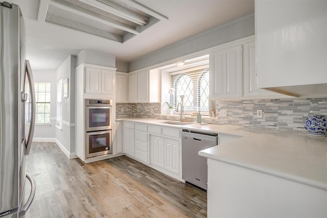 kitchen featuring backsplash, appliances with stainless steel finishes, a sink, light countertops, and white cabinets