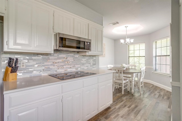 kitchen with visible vents, tasteful backsplash, stainless steel microwave, black electric stovetop, and white cabinetry