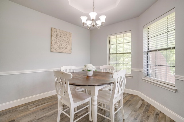 dining space featuring an inviting chandelier, baseboards, a tray ceiling, and wood finished floors