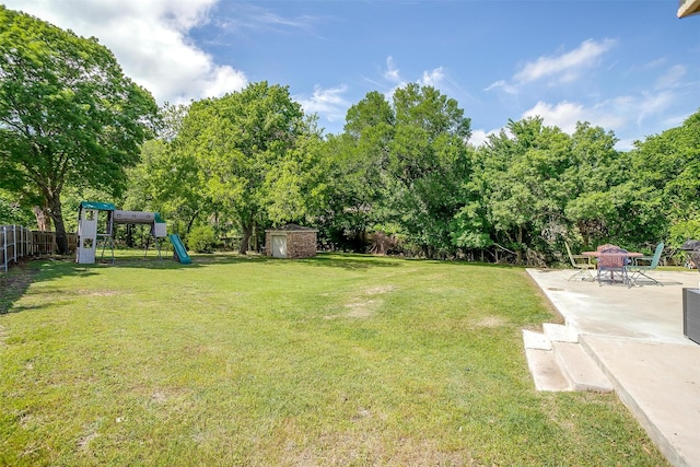 view of yard featuring an outdoor structure, fence, a patio, a storage unit, and playground community