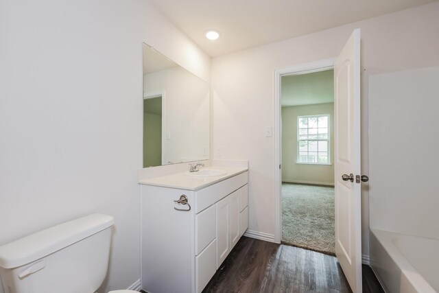 full bathroom featuring a washtub, wood finished floors, vanity, baseboards, and toilet