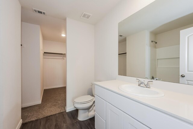 full bath featuring vanity, toilet, wood finished floors, a spacious closet, and visible vents