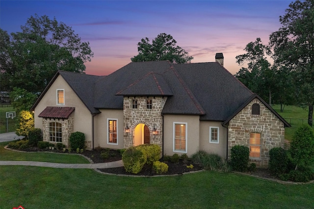 french country style house with a chimney, a front lawn, stucco siding, and stone siding