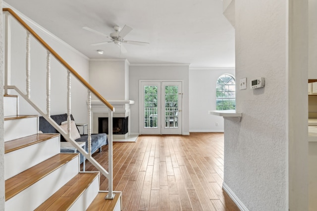 interior space featuring a fireplace with raised hearth, a ceiling fan, wood finished floors, ornamental molding, and stairway