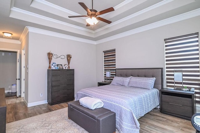 bedroom with baseboards, a tray ceiling, ornamental molding, and wood finished floors