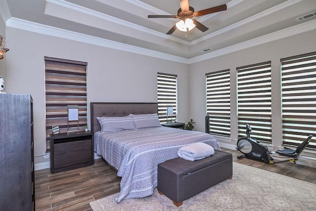 bedroom with ornamental molding, a tray ceiling, wood finished floors, and visible vents