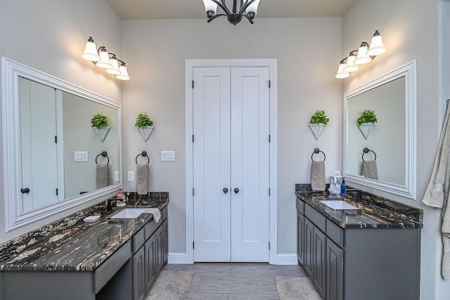 full bath with baseboards, a sink, two vanities, and an inviting chandelier