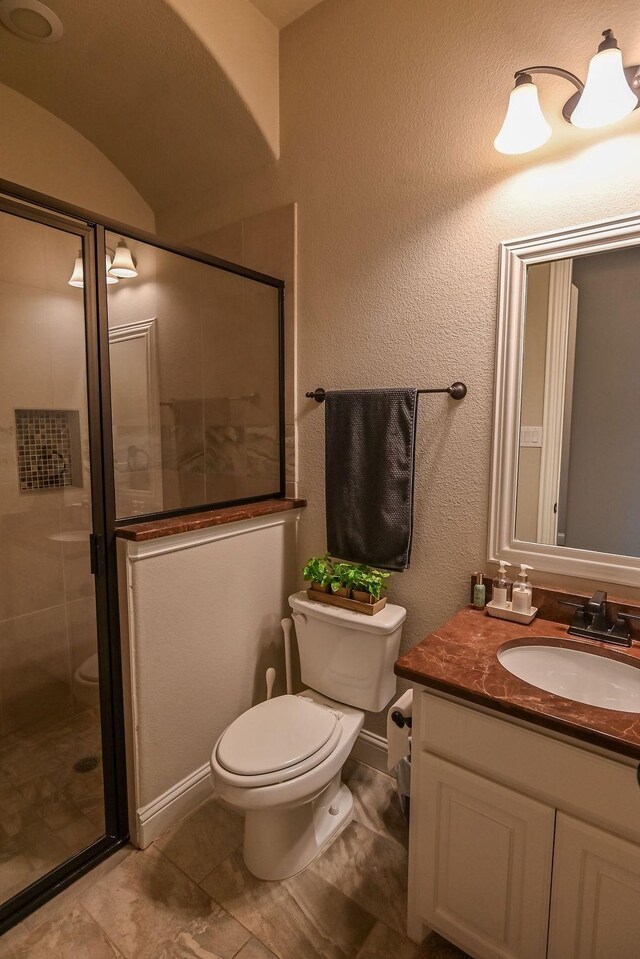 bathroom with a textured wall, tile patterned flooring, vanity, toilet, and a stall shower