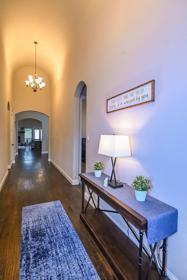 entryway with baseboards, arched walkways, wood finished floors, and a chandelier