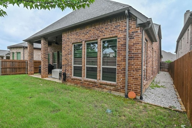 rear view of property with a fenced backyard, brick siding, a shingled roof, a patio area, and a lawn