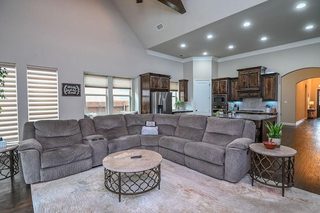living room featuring crown molding, arched walkways, wood finished floors, and high vaulted ceiling