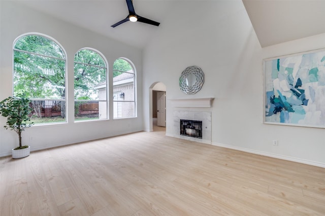 unfurnished living room with wood finished floors, baseboards, arched walkways, a tiled fireplace, and a ceiling fan