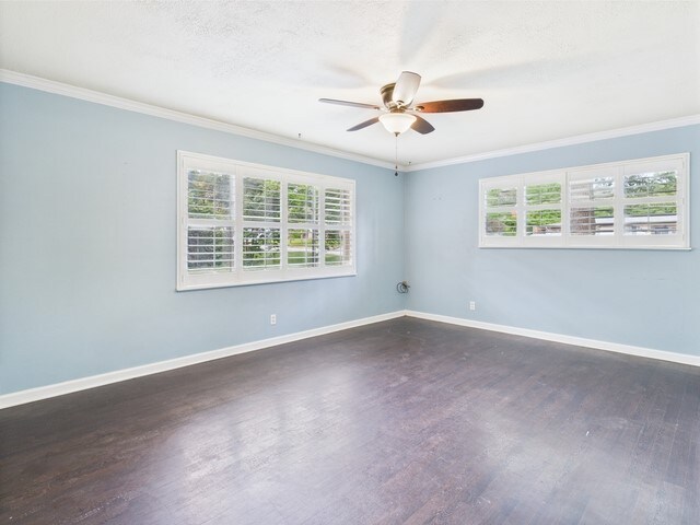 empty room featuring ornamental molding, ceiling fan, dark wood-style floors, and a healthy amount of sunlight
