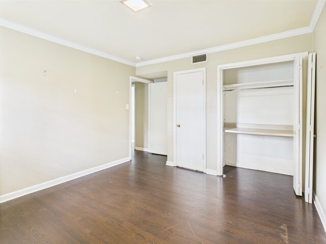 unfurnished bedroom with visible vents, ornamental molding, baseboards, and wood finished floors