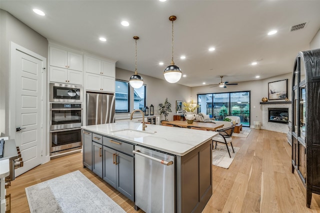 kitchen featuring appliances with stainless steel finishes, a sink, white cabinetry, open floor plan, and visible vents