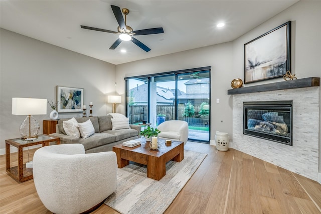 living area with ceiling fan, a stone fireplace, recessed lighting, and wood finished floors