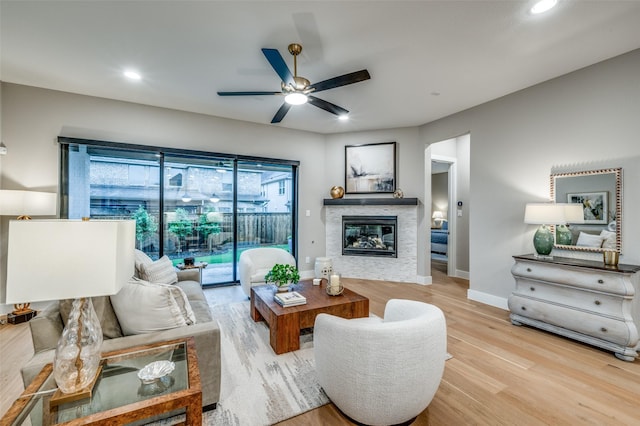 living room featuring recessed lighting, light wood finished floors, ceiling fan, and a stone fireplace