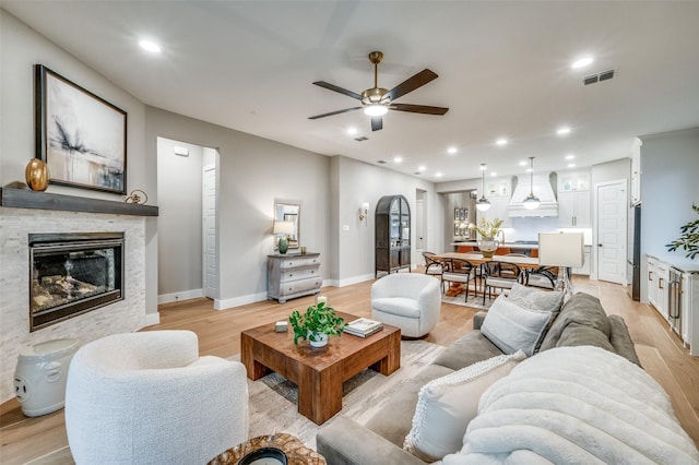 living room featuring ceiling fan, a glass covered fireplace, light wood-style flooring, baseboards, and visible vents