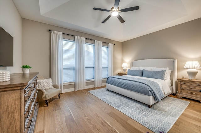 bedroom with light wood-style floors, a ceiling fan, baseboards, and a tray ceiling