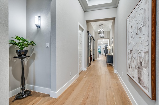 hallway featuring baseboards, ornamental molding, light wood-style flooring, and a barn door