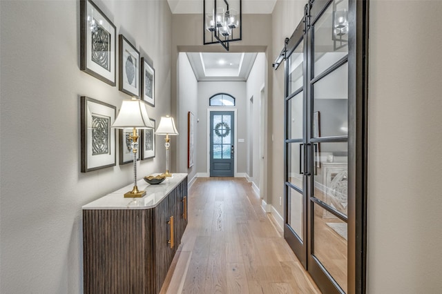 entryway with an inviting chandelier, a barn door, baseboards, light wood-style floors, and a tray ceiling