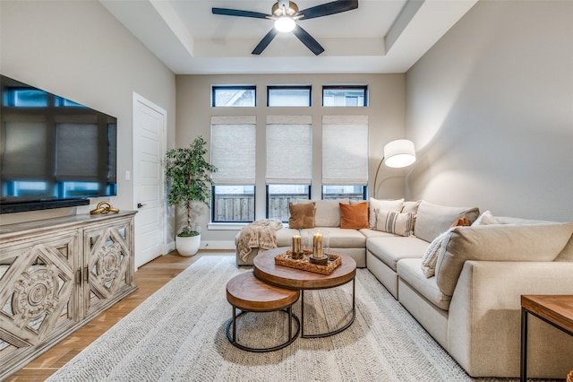 living area with a tray ceiling, ceiling fan, and light wood finished floors