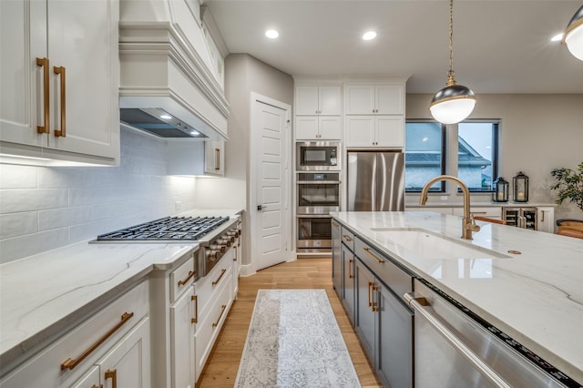 kitchen with white cabinets, appliances with stainless steel finishes, a sink, custom range hood, and gray cabinetry