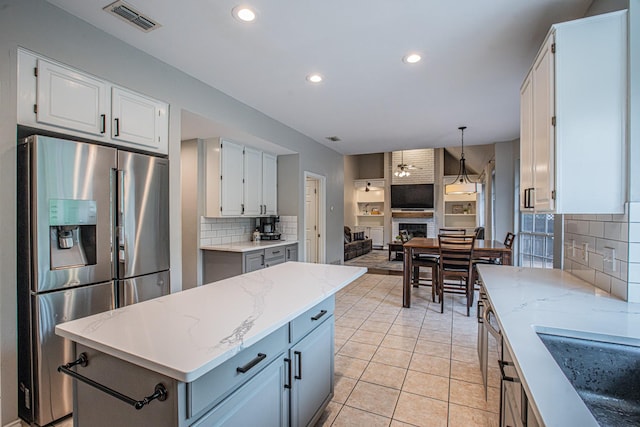 kitchen with a large fireplace, white cabinetry, backsplash, stainless steel refrigerator with ice dispenser, and visible vents