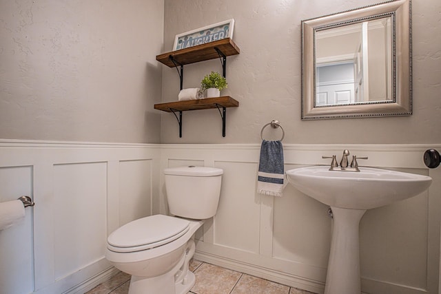 half bath with a decorative wall, toilet, tile patterned flooring, and a wainscoted wall