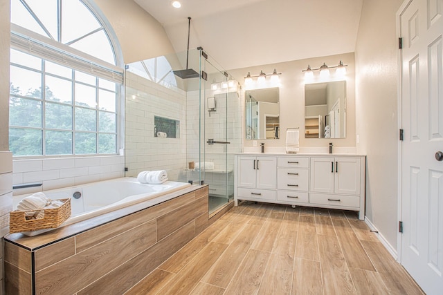 bathroom featuring double vanity, a bath, a shower stall, vaulted ceiling, and wood finished floors