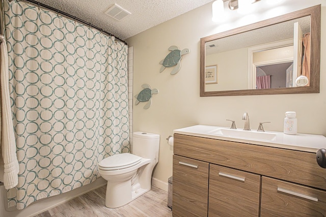 bathroom with vanity, toilet, a textured ceiling, wood finished floors, and visible vents