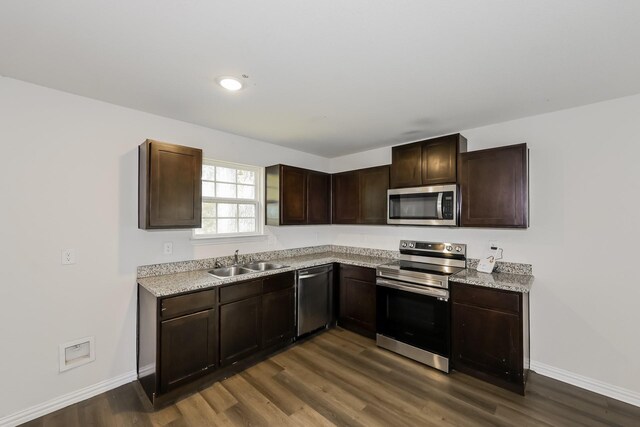 kitchen featuring dark brown cabinetry, appliances with stainless steel finishes, a sink, baseboards, and dark wood-type flooring