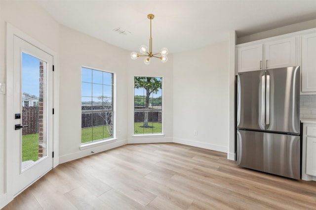 kitchen with an inviting chandelier, light wood-style floors, white cabinets, and freestanding refrigerator