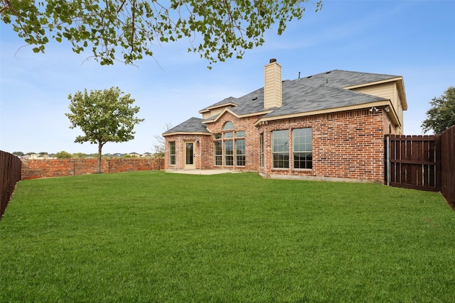 rear view of house with a fenced backyard, a chimney, brick siding, a patio area, and a lawn