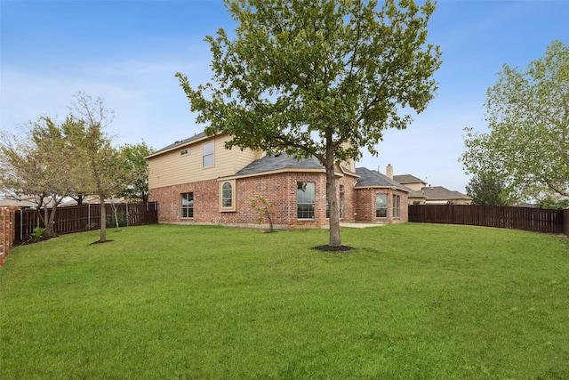 rear view of house with a lawn, brick siding, a fenced backyard, and roof with shingles