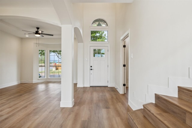 living room with a brick fireplace, high vaulted ceiling, arched walkways, a ceiling fan, and light wood finished floors