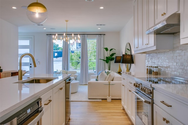 kitchen with visible vents, high end stove, light wood-type flooring, a sink, and under cabinet range hood