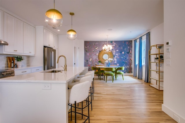 kitchen with wallpapered walls, light wood-type flooring, high quality appliances, white cabinets, and a sink
