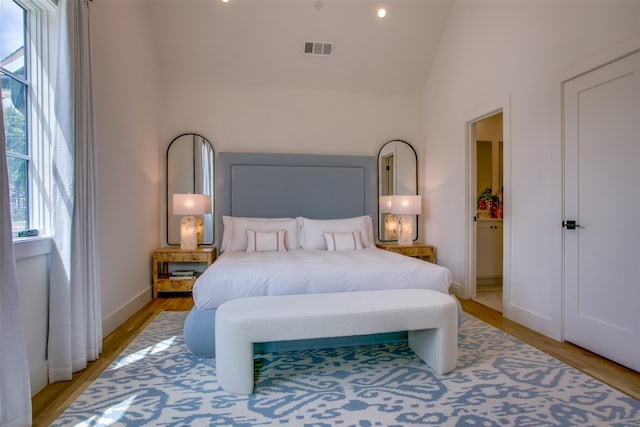 bedroom featuring baseboards, vaulted ceiling, light wood finished floors, and visible vents