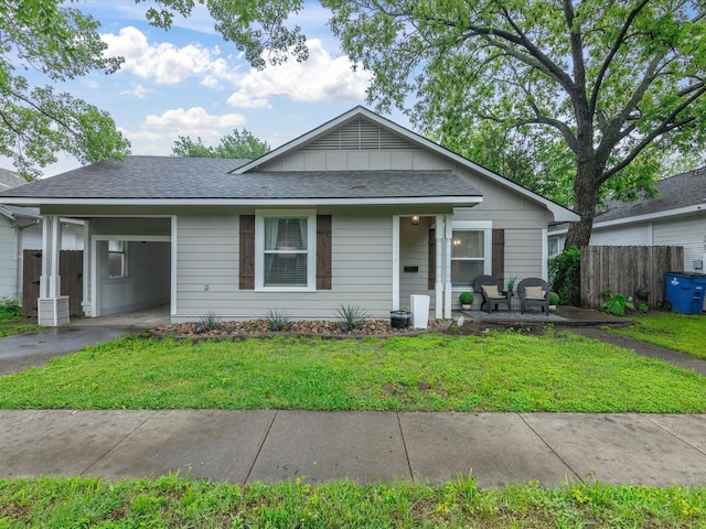 view of front of home with fence, board and batten siding, an attached carport, and a front yard