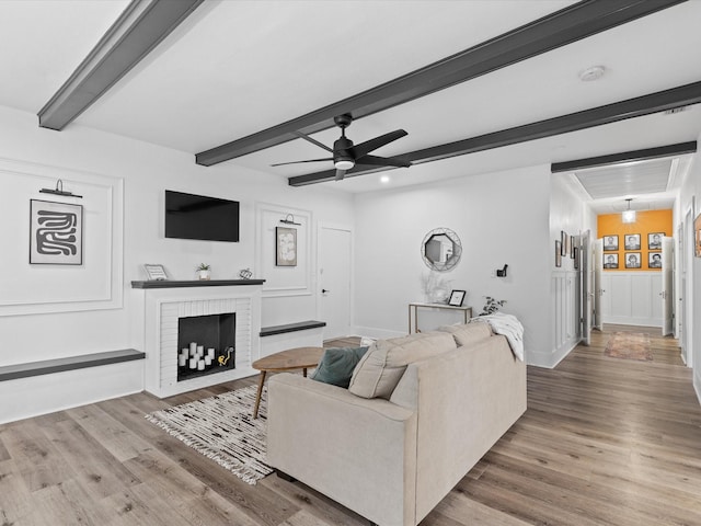 living area featuring a ceiling fan, beamed ceiling, wood finished floors, and a fireplace