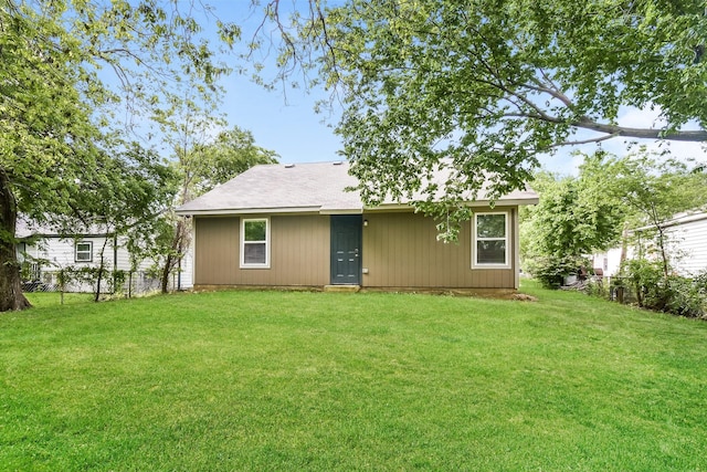 rear view of property featuring a lawn and fence