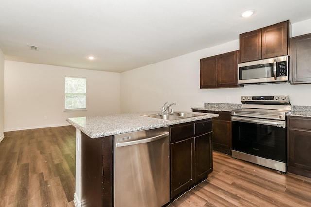 kitchen with a sink, appliances with stainless steel finishes, wood finished floors, and an island with sink
