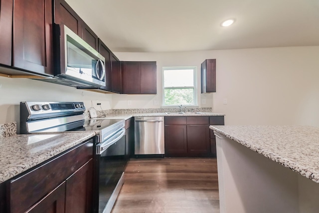 kitchen with dark wood-style flooring, dark brown cabinetry, appliances with stainless steel finishes, light stone counters, and a sink