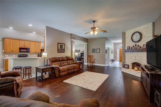 living area featuring a fireplace, arched walkways, a ceiling fan, baseboards, and dark wood-style floors