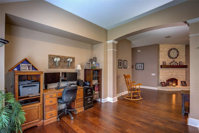 office featuring dark wood-type flooring, arched walkways, baseboards, and a stone fireplace